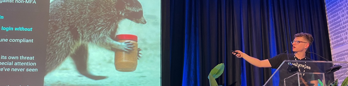 Man presenting onstage with a raccoon carrying a peanut butter jar on the slide